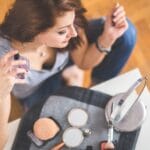 Młoda kobieta aplikuje perfumy, obok leżą kosmetyki do makijażu