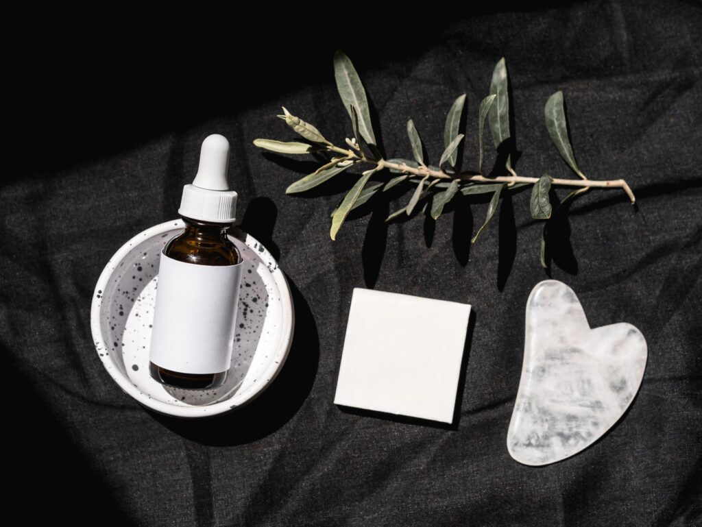 Butelka serum z pipetą i płytka gua sha na czarnym tle