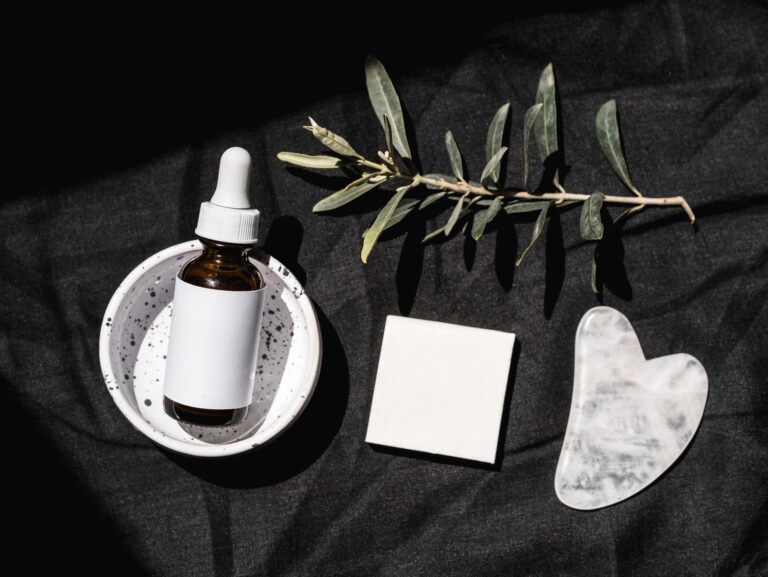 Butelka serum z pipetą i płytka gua sha na czarnym tle